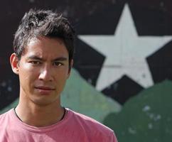 jonge Euraziatische volwassene die met een zelfverzekerde en serieuze blik in de camera kijkt, terwijl hij voor een muur staat met een ster erop. foto