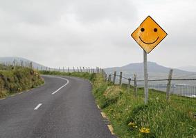 optimisme - geel verkeersbord met smiley voor een bocht in een heuvelachtig landschap foto