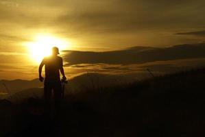 donker silhouet van een jonge man met een hoed in de laatste minuten voordat de zon ondergaat. foto