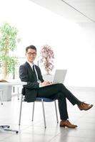 jonge Aziatische zakenman met behulp van tablet, mobiele telefoon op kantoor foto