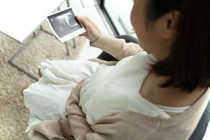 Aziatische zwangere vrouw die thuis naar echografie kijkt foto