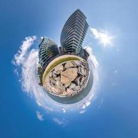 kleine planeet in blauwe lucht met wolken in het centrum in de buurt van moderne wolkenkrabbers of kantoorgebouwen. transformatie van bolvormig 360 panorama in abstracte luchtfoto. foto