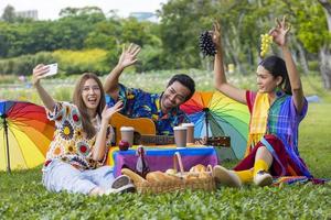 groep jonge diversiteit lgbtq-vrienden die picknicken in de tuin terwijl ze genieten van het zingen van muziek in het openbare openluchtpark in de zomer met vreugde en geluk foto