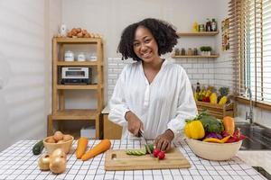 Afro-Amerikaanse huisvrouw hakt biologische komkommer om een eenvoudige en gemakkelijke salademaaltijd in zuidelijke stijl te bereiden voor een veganistisch en vegetarisch voedselconcept foto