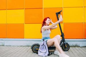 vrouw gebruikt een smartphone en een elektrische scooter in de zomer in de stad foto