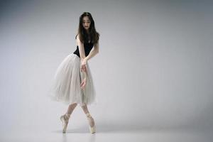 een ballerina in een bodysuit en een witte rok improviseert klassieke en moderne choreografieën in een fotostudio foto