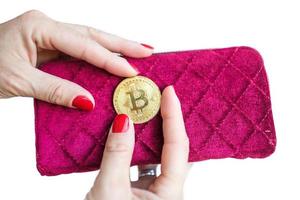 virtueel geld gouden bitcoin op roze vrouwen stoffen portemonnee. vingers met rode spijkers op een muntstuk dat op witte achtergrond wordt geïsoleerd foto
