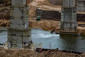 bouw of reconstructie van een betonnen snelwegbrug over een brede rivier. bouwmachines, vrachtwagens en kranen werken foto