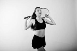 zwart-wit portret van een mooie jonge vrouw in sportkleding die een tennisracket vasthoudt terwijl hij tegen een witte achtergrond staat. foto