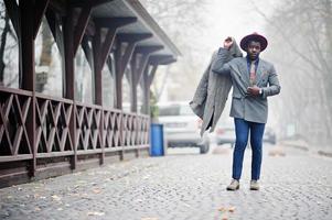 stijlvolle Afro-Amerikaanse man model in grijze jas, jas stropdas en rode hoed gesteld op mistig weer straat. foto