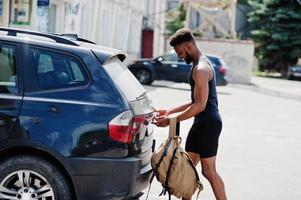 Afro-Amerikaanse mannelijke atleet sport man met rugzak tegen zijn zwarte SUV-auto voor de training. foto