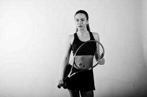 zwart-wit portret van een mooie jonge vrouw in sportkleding die een tennisracket vasthoudt terwijl hij tegen een witte achtergrond staat. foto