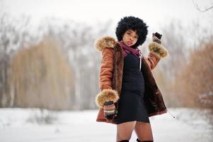 krullend haar Afro-Amerikaanse vrouw dragen op schapenvacht jas en handschoenen gesteld op winterdag. foto