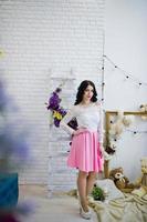 jonge brunette meisje in roze rok en witte blouse poseerde binnen tegen kamer met speelgoed beer. foto