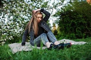 jonge brunette meisje op jeans zittend op plaid tegen lente bloesem boom. foto