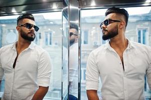 stijlvolle lange Arabische man model in wit overhemd en zonnebril poseerde bij lift binnen. foto