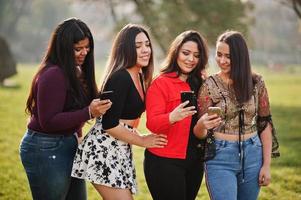 groep van vier gelukkige en mooie latino-meisjes uit ecuador poseerden op straat en kijken naar mobiele telefoons. foto