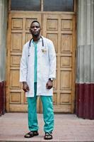 Afro-Amerikaanse dokter man bij laboratoriumjas met stethoscoop buiten tegen kliniek deur. foto