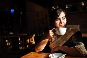 elegante brunette Zuid-Aziatische Indiase meisje in saree poseerde indoor cafe en thee drinken. foto