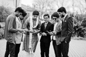 groep van zes Zuid-Aziatische Indiase mannen in traditionele, casual en zakelijke kleding die samen naar mobiele telefoons kijken. foto