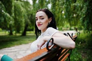 brunette meisje in groene rok en witte blouse gesteld op park, zittend op een bankje. foto