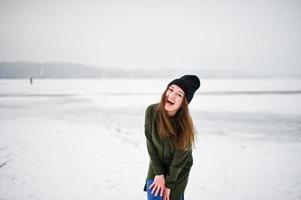 grappige meisjesslijtage op lang groen sweatshirt, jeans en zwarte hoofddeksels, bij bevroren meer in de winterdag. foto