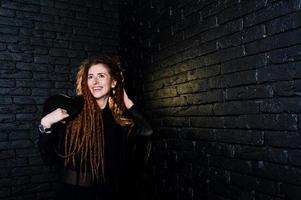 studio shoot van meisje in het zwart met dreadlocks en hoed op bakstenen achtergrond. foto