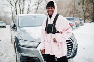 stijlvolle stedelijke stijl Afro-Amerikaanse man in roze hoodie poseerde tegen suv-auto in de winter. Afro-rapper kerel. foto