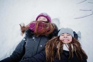 twee grappige meisjes vrienden plezier op besneeuwde winterdag in de buurt van besneeuwde bomen. foto