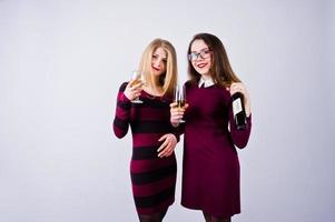 twee aantrekkelijke vrienden in paarse jurken drinken mousserende wijn of champagne in de studio. foto