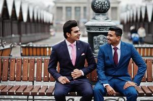 twee elegante Indiase modieuze mans model op pak gesteld op winterdag zittend op de bank. foto