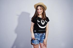 portret van een aantrekkelijk meisje in een zwart t-shirt met de tekst lol, denim shorts, hoed en zonnebril poseren in de studio. foto