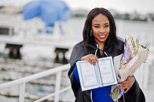 Afro-Amerikaanse student meisje in zwarte toga afstuderen met diploma, op blauwe pak gesteld. foto