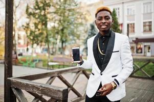 chique knappe Afro-Amerikaanse man in wit pak met mobiele telefoon bij de hand. foto