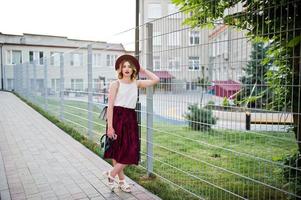 modieuze en mooie blonde model meisje in stijlvolle rood fluwelen velours rok, witte blouse en hoed, gesteld met telefoon en koptelefoon. foto