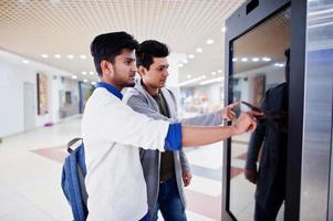 twee aziatische jongens die het scherm van de elektronische informatiebalie in het winkelcentrum aanraken. foto