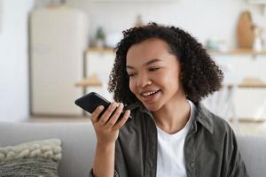 vriendelijk afro-amerikaans jong meisje houd smartphone vast laat een spraakbericht achter of gebruik virtuele assistent foto