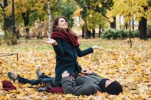 mooie vrouw heeft plezier met vriendje, gooit gele bladeren, zit op de man, brengt tijd samen door in het herfstpark, heeft gelukkige uitdrukkingen. emotionele vriendin verheugen zich op saamhorigheid. relatie concept foto