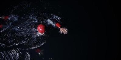 triatlonatleet die in donkere nacht zwemt die wetsuit draagt foto
