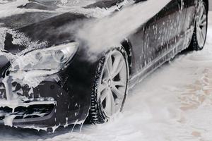 zwarte auto gewassen door hoge druk van water en zeep bij carwash. schoonmaak dienstverleningsconcept. zelfbediening autowasstation foto