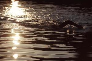 triatlonatleet die op meer in zonsopgang zwemt die wetsuit draagt foto