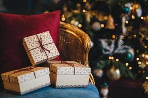 foto van verpakte geschenkdozen liggen op fauteuil tegen versierde nieuwjaarsboom achtergrond. voorbereiding op vakantie. mooie kerstboom met slingers en cadeautjes binnen