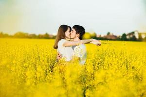 jong verliefd stel omarmen elkaar en hebben een gepassioneerde kus terwijl ze poseren tegen een geel veld met bloemen, waarachtige relaties en toewijding tonen. mensen, liefde en toewijding concept foto