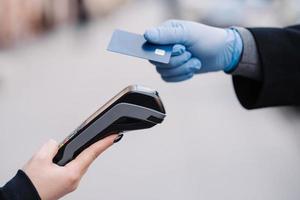 gezichtsloze mens in medische handschoenen tijdens coronavirusepidemie, houdt plastic kaart vast, probeert contant te betalen voor veiligheid, maakt gebruik van moderne technologie. pandemie, virus en preventieconcept foto