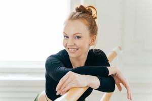 fitness vrouw met rood gekamd haar, draagt speciale kleding, beoefent ballet op barre in dansstudio, heeft een brede glimlach, is opgewekt, draagt make-up, heeft een gezonde levensstijl. trainingsconcept foto