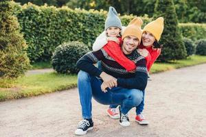 mooie vrouw, klein meisje omarmen hun knappe vader en echtgenoot, hebben een goede relatie, hebben een actieve levensstijl, poseren tegen groene bomen. familie hebben samen lopen, omhelzen elkaar foto