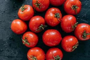 mooie rijpe verse rode tomaten geteeld in kas. waterdruppels op heirloom groenten geïsoleerd op donkere achtergrond. landbouw foto