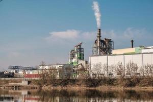 pijpen van houtbewerking onderneming plant zagerij in de buurt van rivier. luchtvervuiling concept. industrieel landschap milieuvervuiling afval van thermische elektriciteitscentrale foto