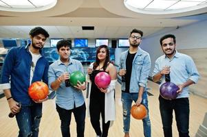 groep van vijf Zuid-Aziatische volkeren die rust en plezier hebben bij de bowlingclub. koude frisdranken uit glazen flessen en bowlingballen bij de hand houden. foto