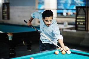 stijlvolle arabische man draagt een spijkerbroek die poolbiljart speelt op de bar. foto